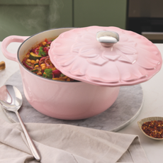 Aldi pink cast iron petal caserole on white kitchen countertop, filled with vegetable stew.