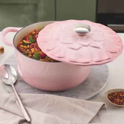 Aldi pink cast iron petal caserole on white kitchen countertop, filled with vegetable stew.