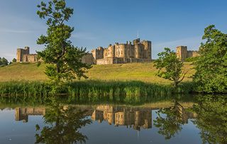 Alnwick Castle reflected in the river Aln on a clear summer's morning, Northumberland, England