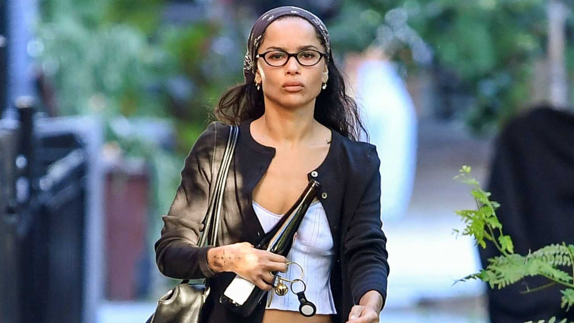 Zoe Kravitz wearing a black cardigan, white tank top, black pants, and black flats