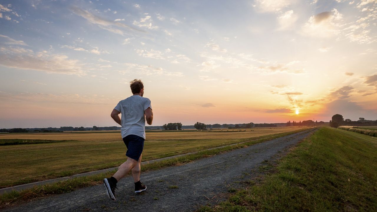 A man in shorts and a t-shirt runs down a gravel road in a rural setting as the sun rises