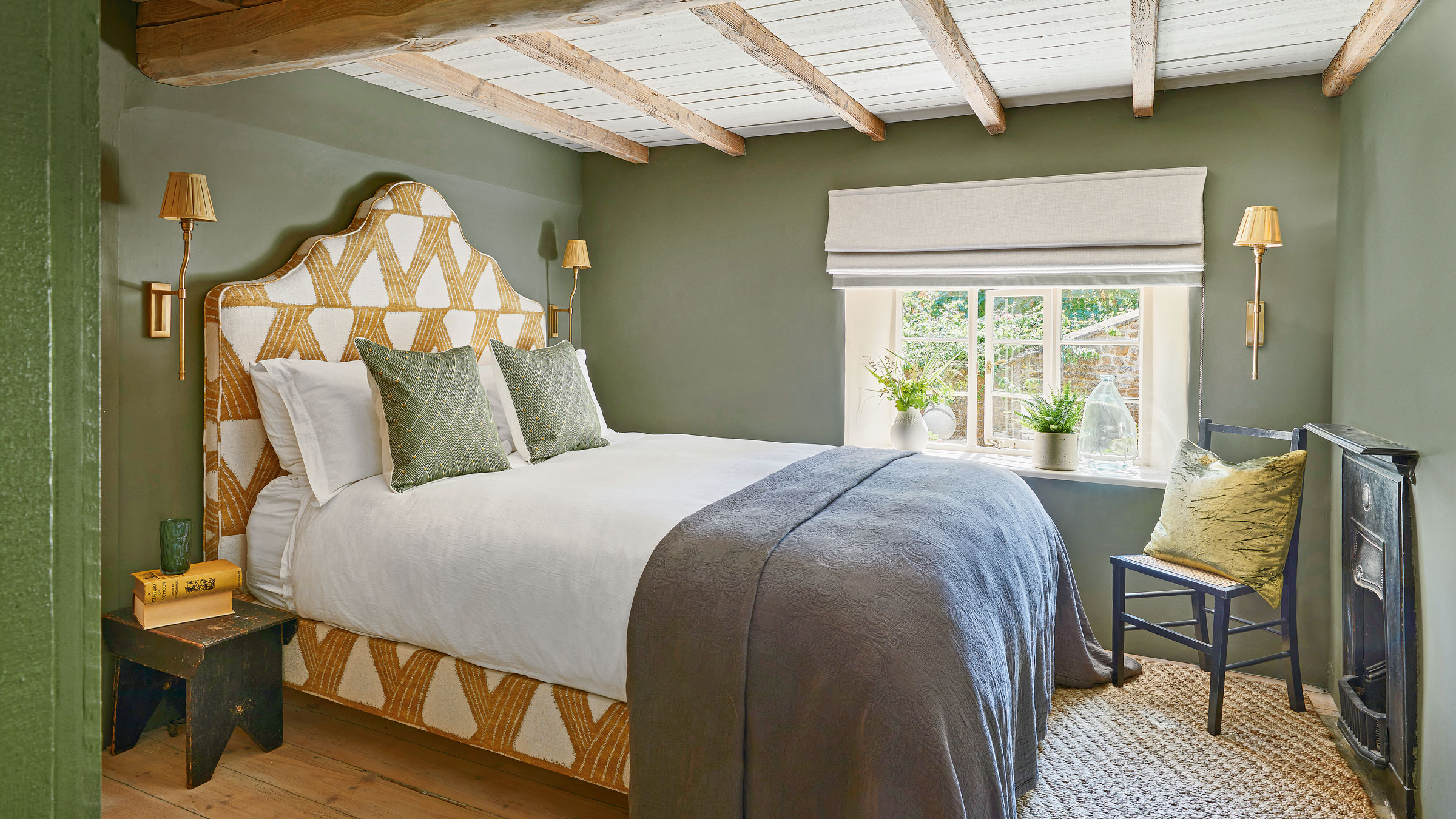 Green bedroom with yellow headboard, wall lights and black chair in the corner