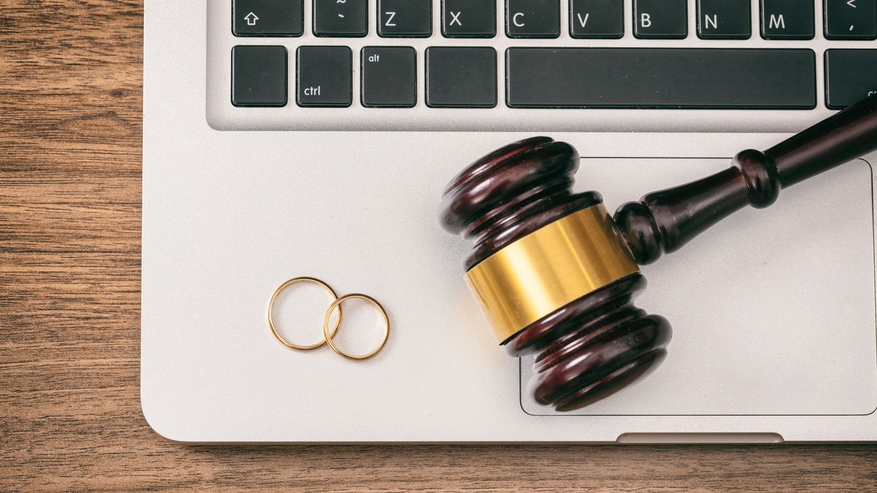 Wedding rings sit on top of a laptop keyboard along with a judge&#039;s gavel.