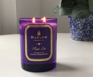 Harlem Candle Co Purple Love lit and burning on a white table with a plant in the background