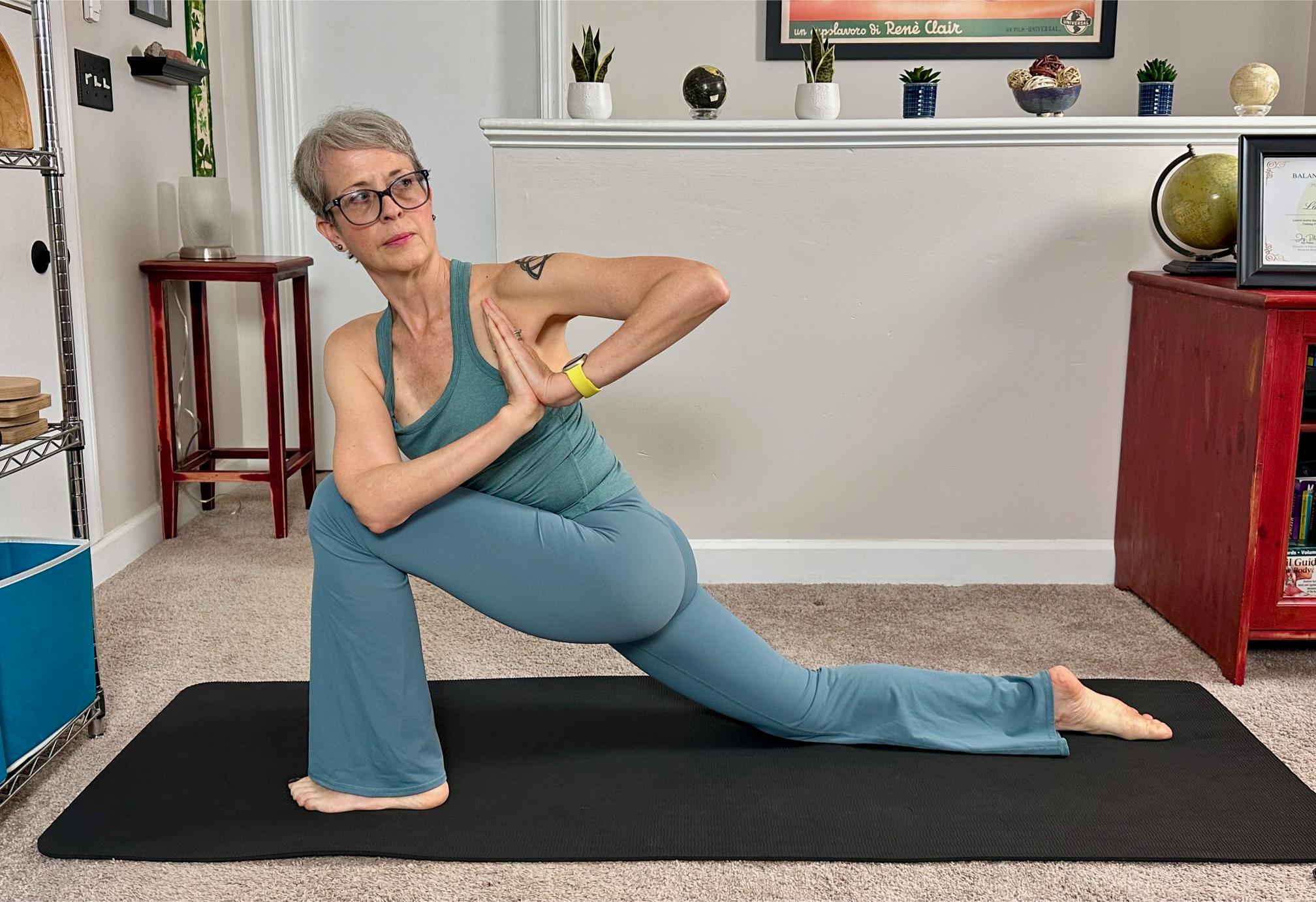 woman performing a low lunge with twist in a living room on a black yoga mat