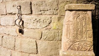 The ancient Pictish symbol stone at the foot of the 11th century Irish Celtic round tower in Abernethy, Scotland. On the left-hand side of the image there are some chains.