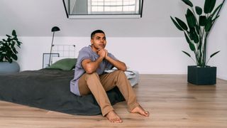 A man sat on the edge of his mattress that's placed on the wooden floor