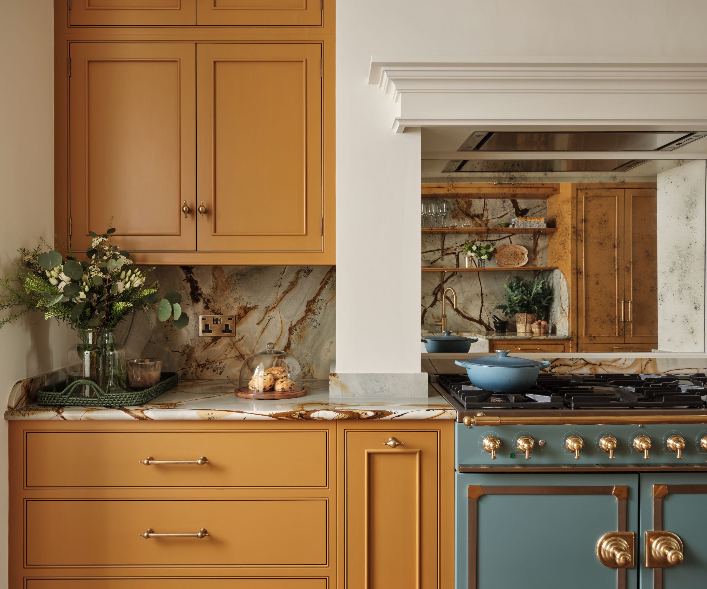 Kitchen with yellow painted cabinetry and drawers, marble countertops and backsplash, blue french range oven with mirror backsplash