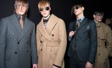 Four men with sweeping hair across their face in coats stood in a dark room lit up by the camera flash