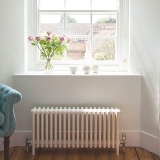 White radiator on the wall underneath a window and windowsill with a vase of flowers on it