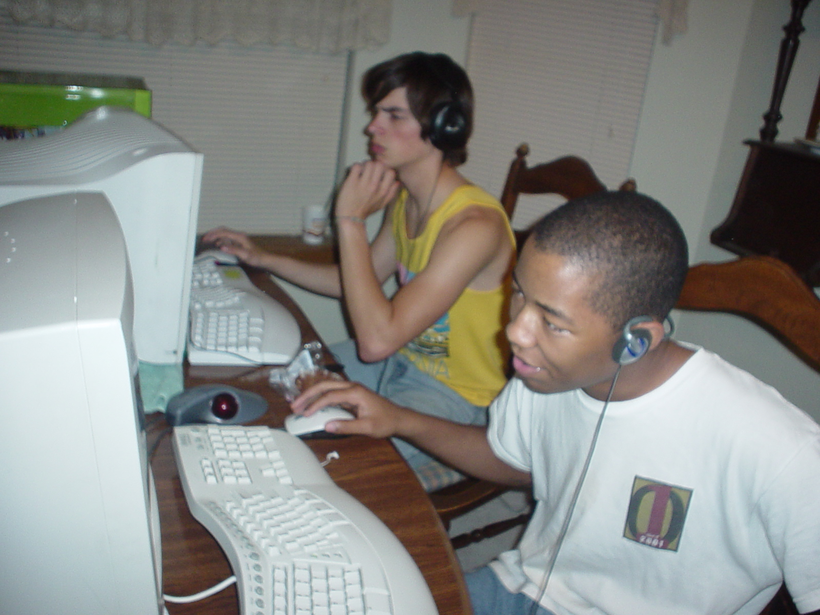 Two teenagers sit side-by-side, absorbed in games on unseen CRT monitor screens.