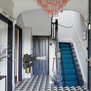 hallway with monochrome floor tiles, stairs with blue runner and pink chandelier