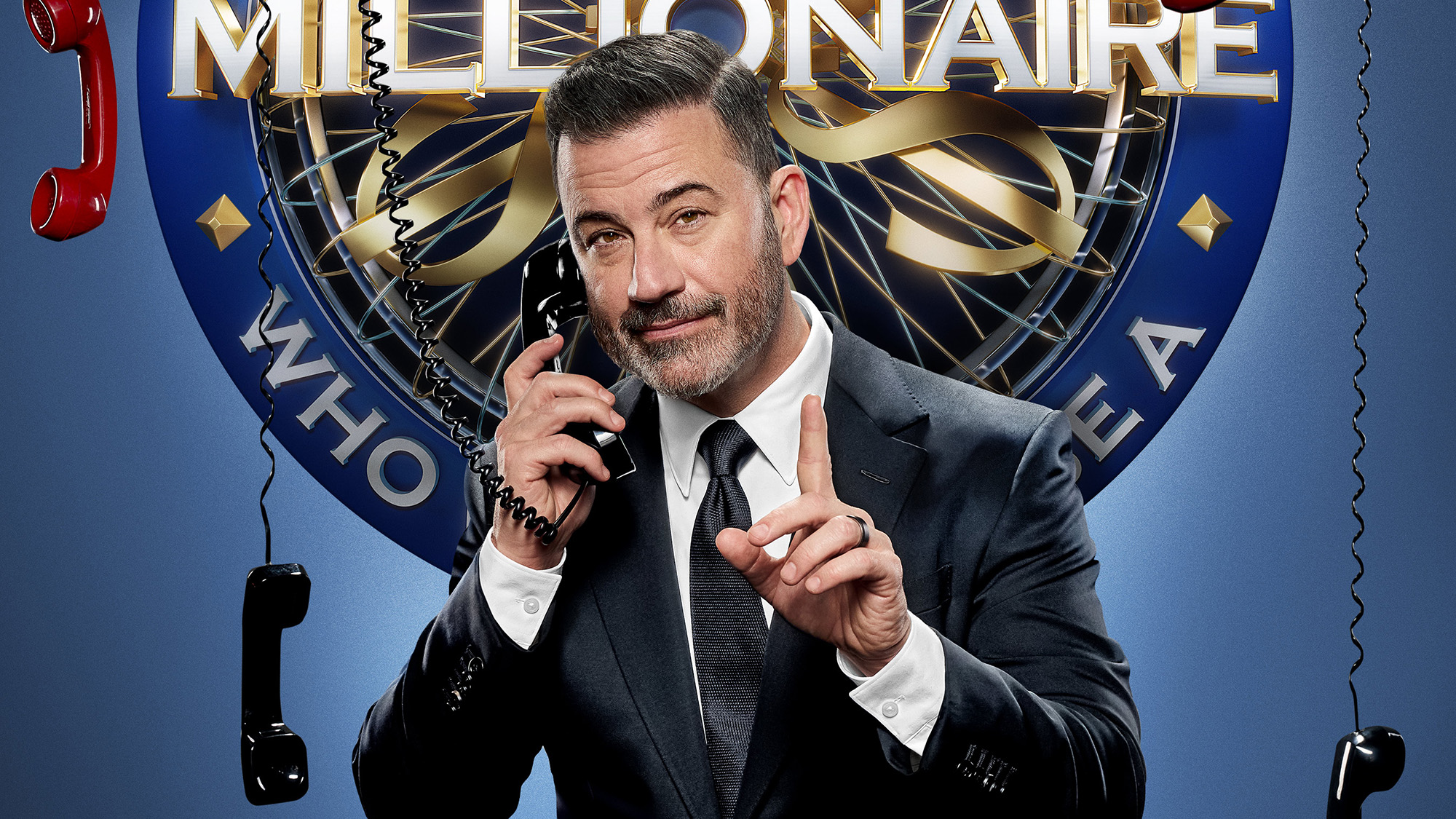 Jimmy Kimmel pretending to talk on the phone while wearing a suit and rocking a side part for Who Wants To Be A Millionaire.