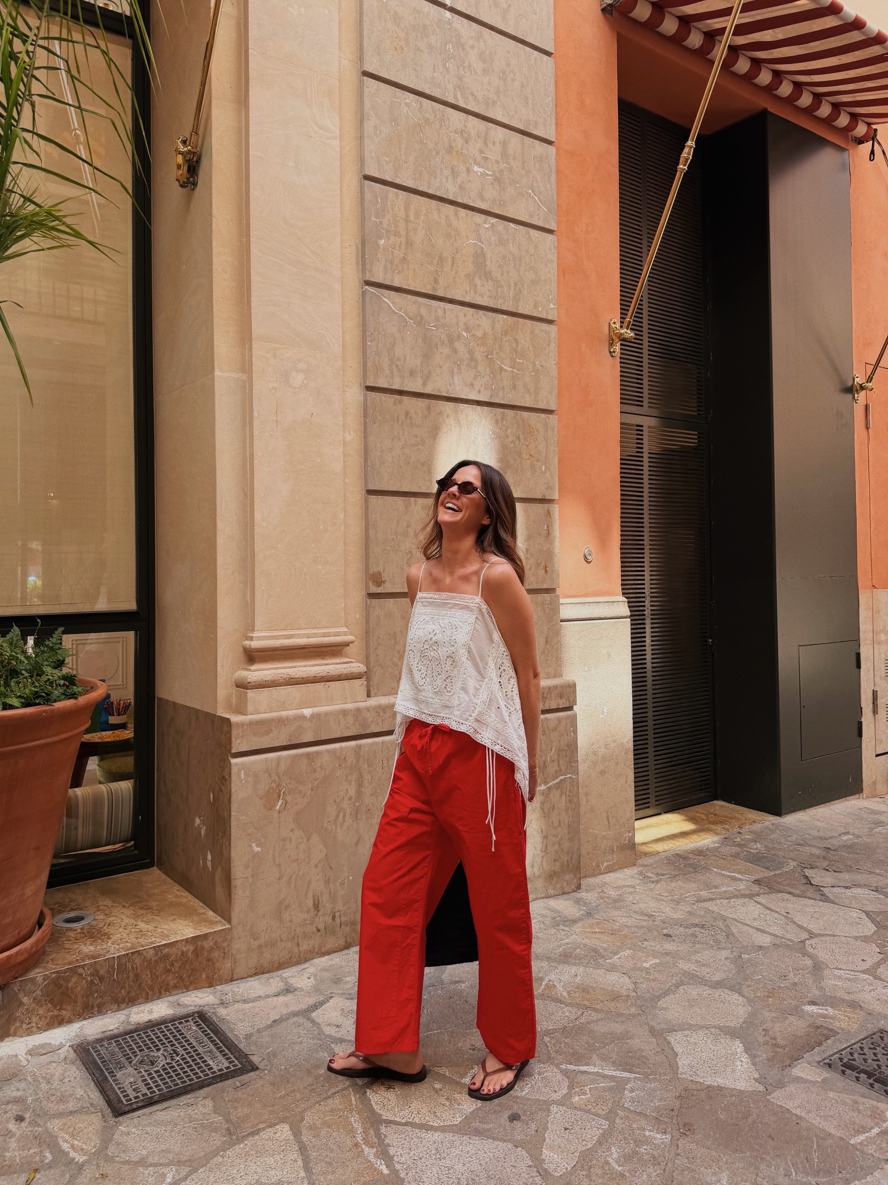 An image of an influencer wearing a white sleeveless top, red cotton poplin trousers and black flip-flops.