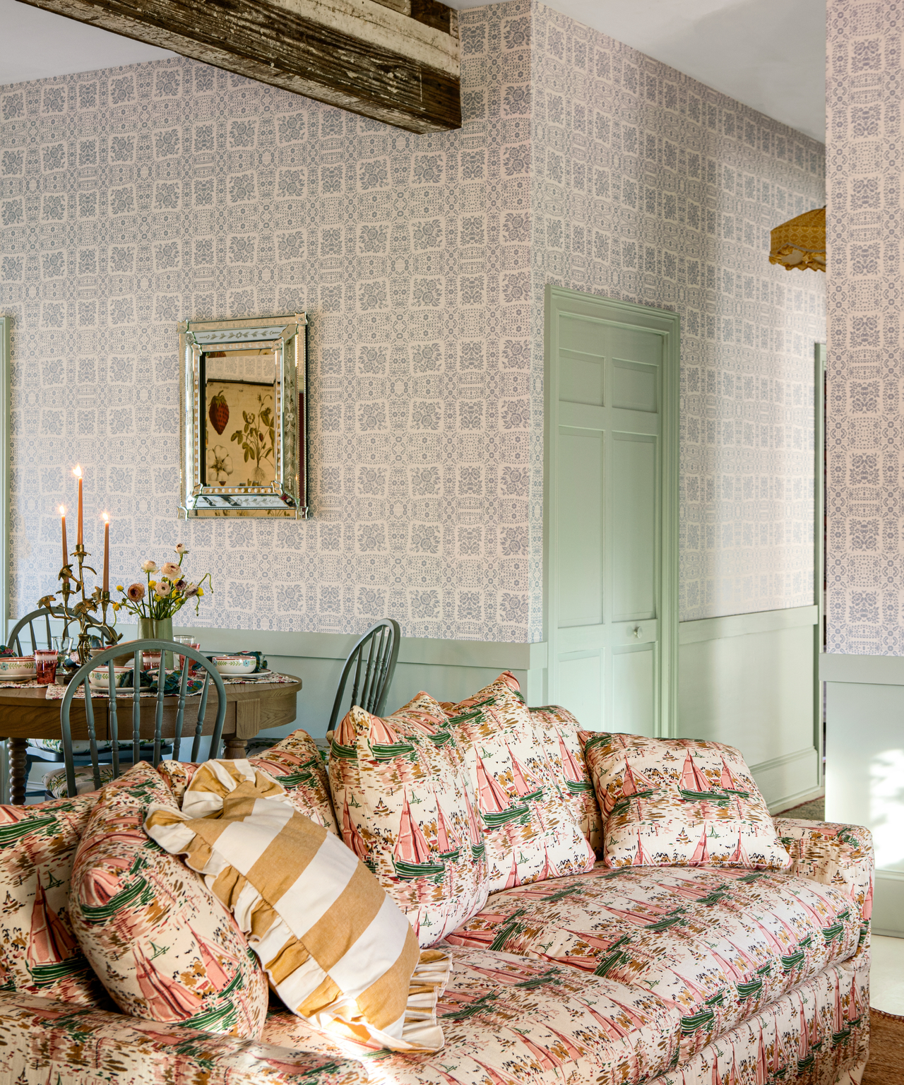 a living room with a large printed couch, a small dining table behind it, blue printed wallpaper, and mint green paint