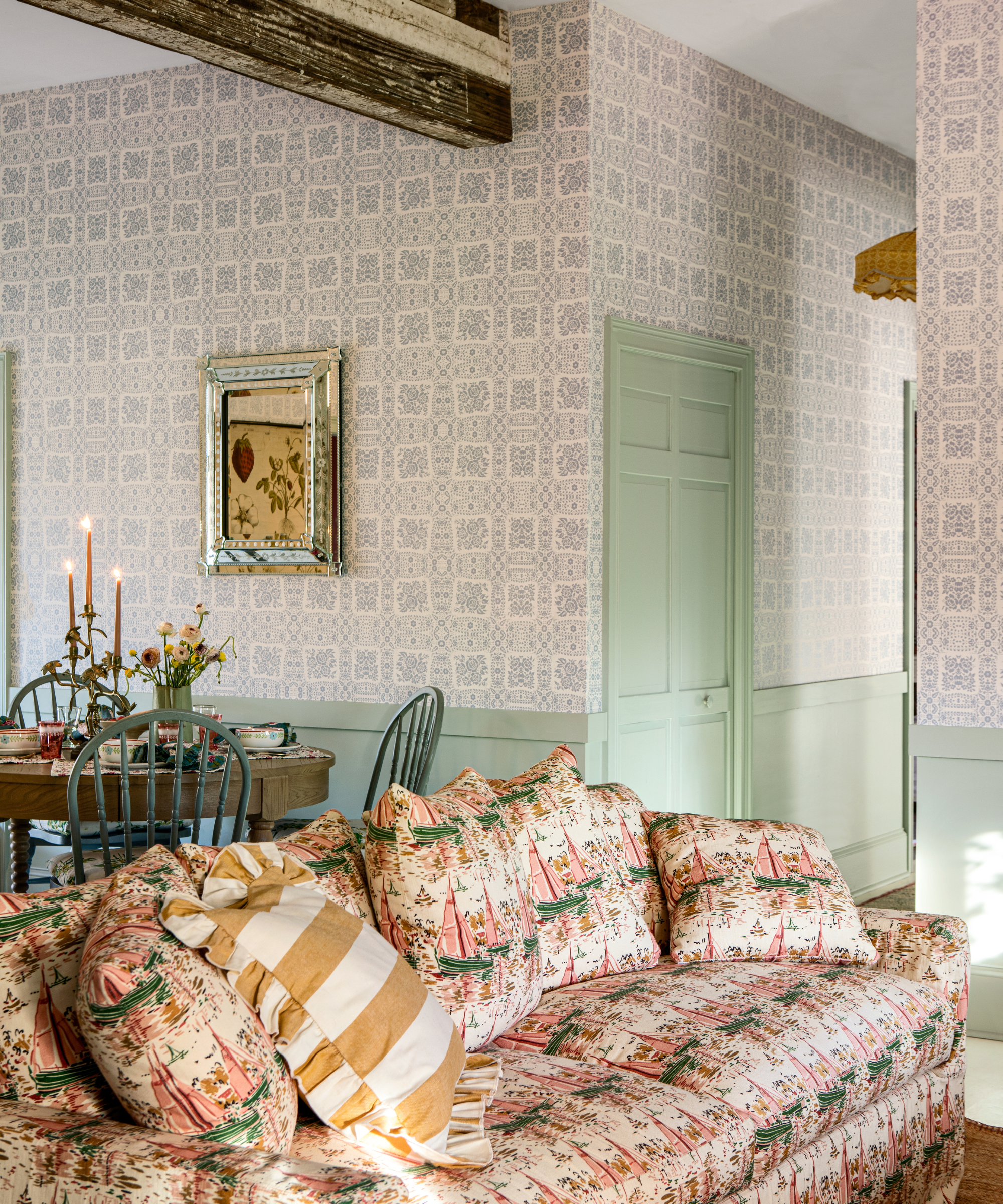 a living room with a large printed couch, a small dining table behind it, blue printed wallpaper, and mint green paint 