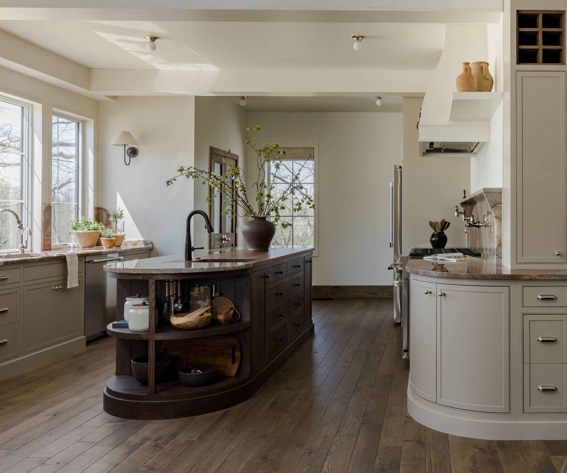 A large kitchen with white cabinets, mid-tone wooden floors and a curved dark wood island