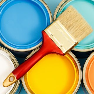 cans of different colored paint with a red paintbrush on top