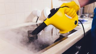 A yellow steam cleaner being used on an electric cooktop