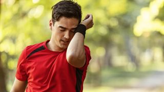 Man wiping away sweat while running in woods