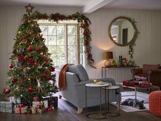 Christmas living room with large tree, baubles, animal decorations, poinsettia decorations, garland, sofa, presents wrapped