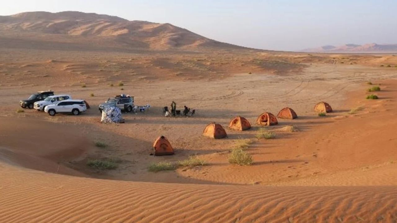 A line of orange tents in the desert with a mountain in the background.