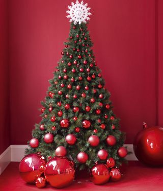 Green christmas tree with red baubles and white snowflake on top in red room