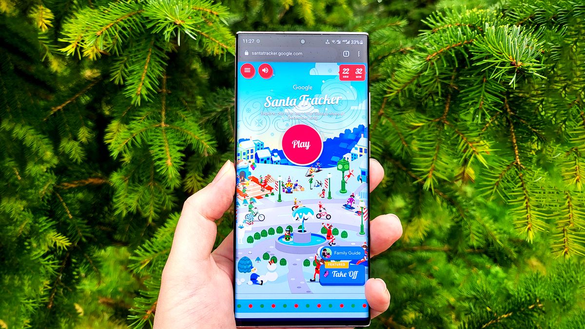 Smartphone with Google&#039;s Santa Tracker webpage open being held in front of pine trees