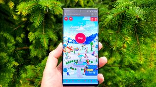 Smartphone with Google's Santa Tracker webpage open being held in front of pine trees
