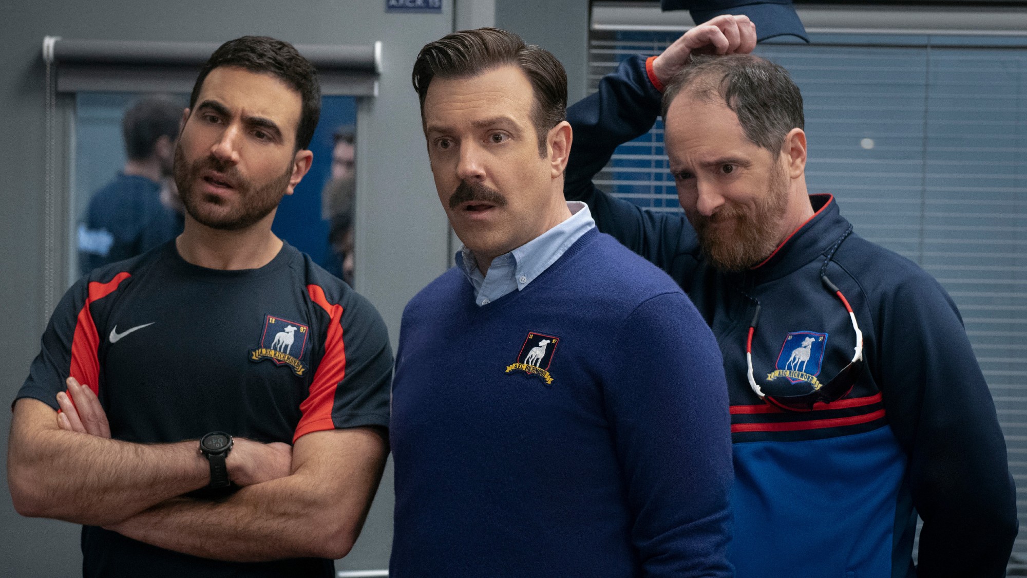 From left to right: Brett Goldstein folding his arms, Jason Sudeikis standing and Brendan Hunt scratching his head. They all look confused. 