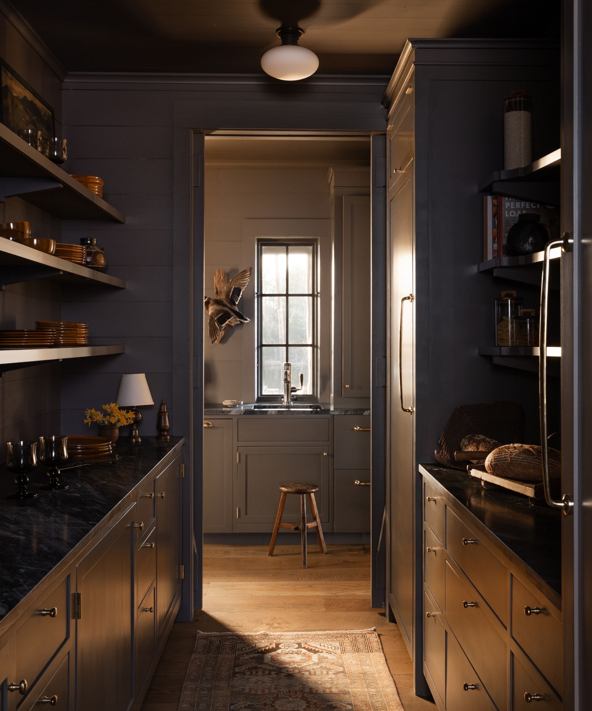Color-drenched pantry with dark cabinetry, marble countertops, open shelving, and a window above the sink.
