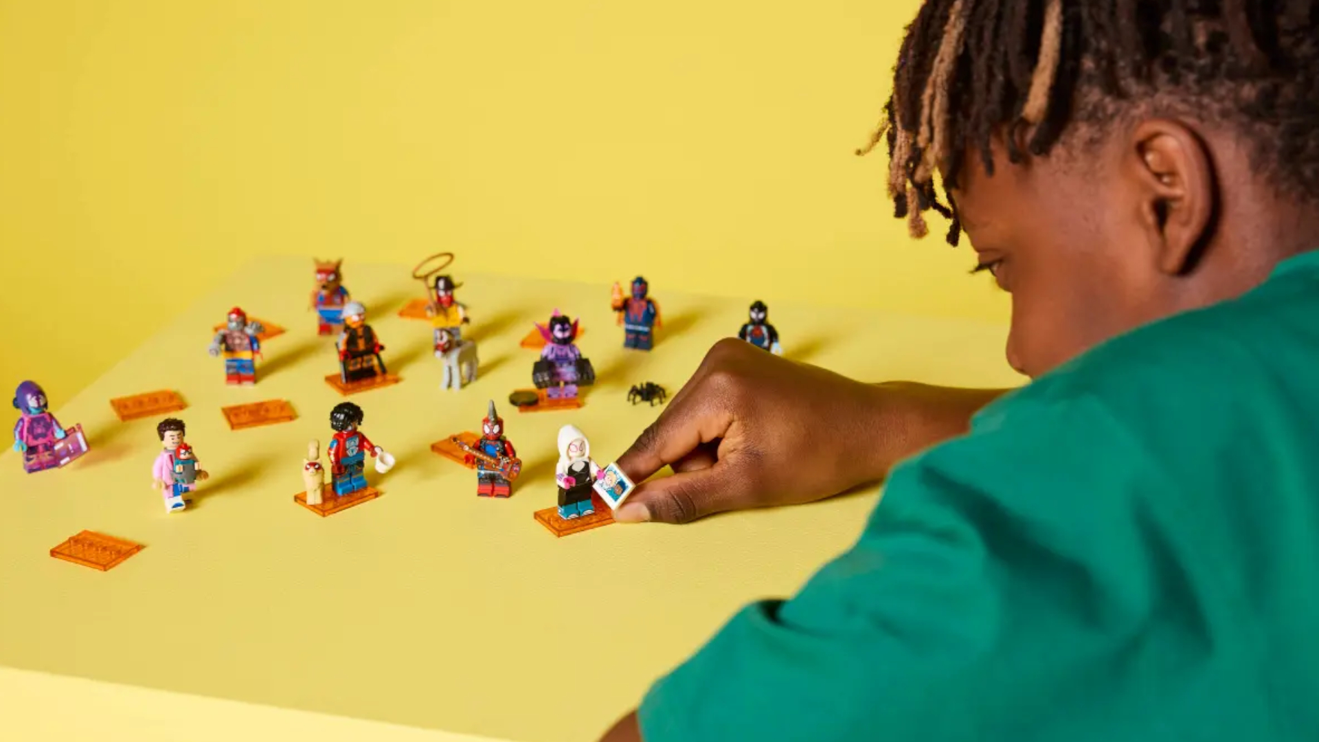 A boy places a Ghost Spider minifigure on a yellow surface