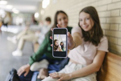 A high school student showing a selfie of her and a friend to the camera.