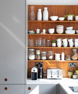 wooden open shelving in a grey modern kitchen with glassware and ceramics piled high