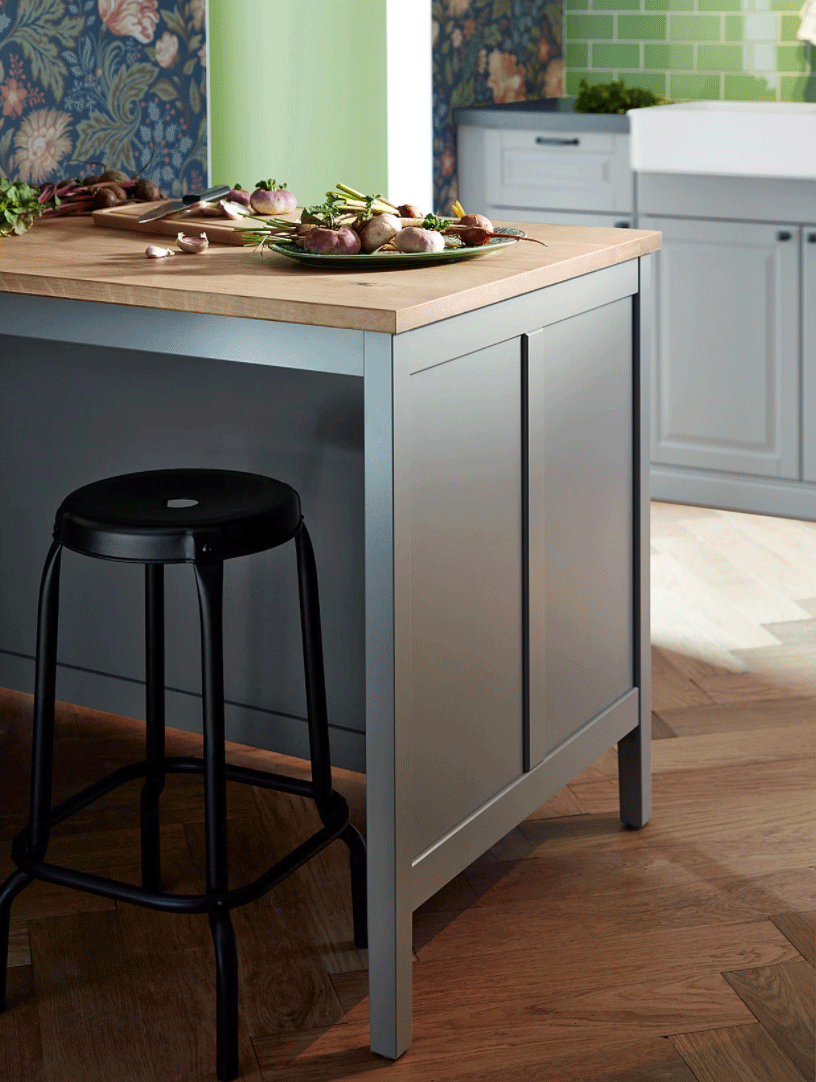 A gray portable kitchen island with simple black bar stools in a kitchen with herringbone flooring