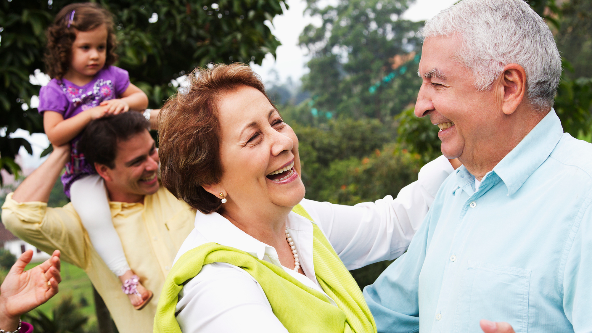 Two old people dance together with younger family members in the background
