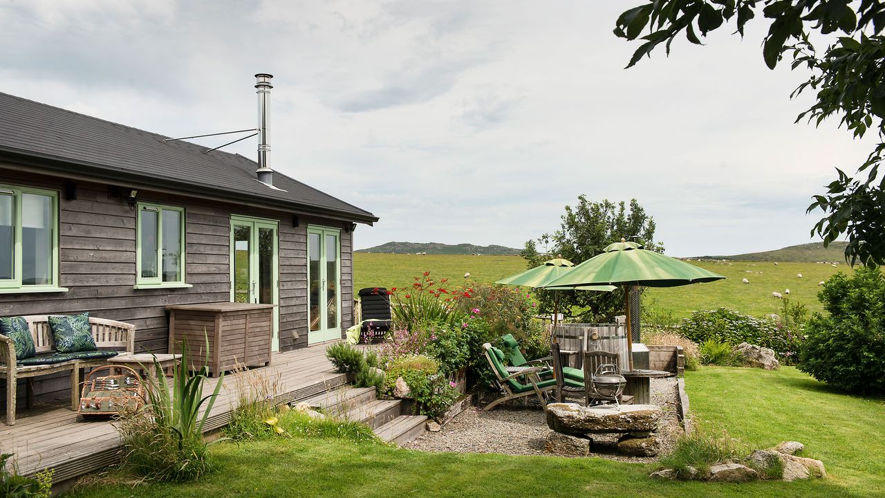 Exterior of wooden built Cornish cabin set in green fields with green parasols