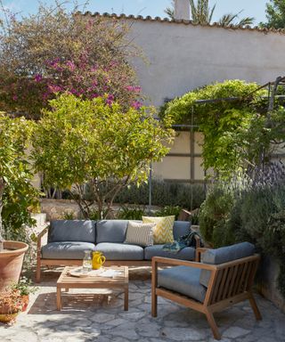 A small backyard patio area with large trees and outdoor 3-seater sofa