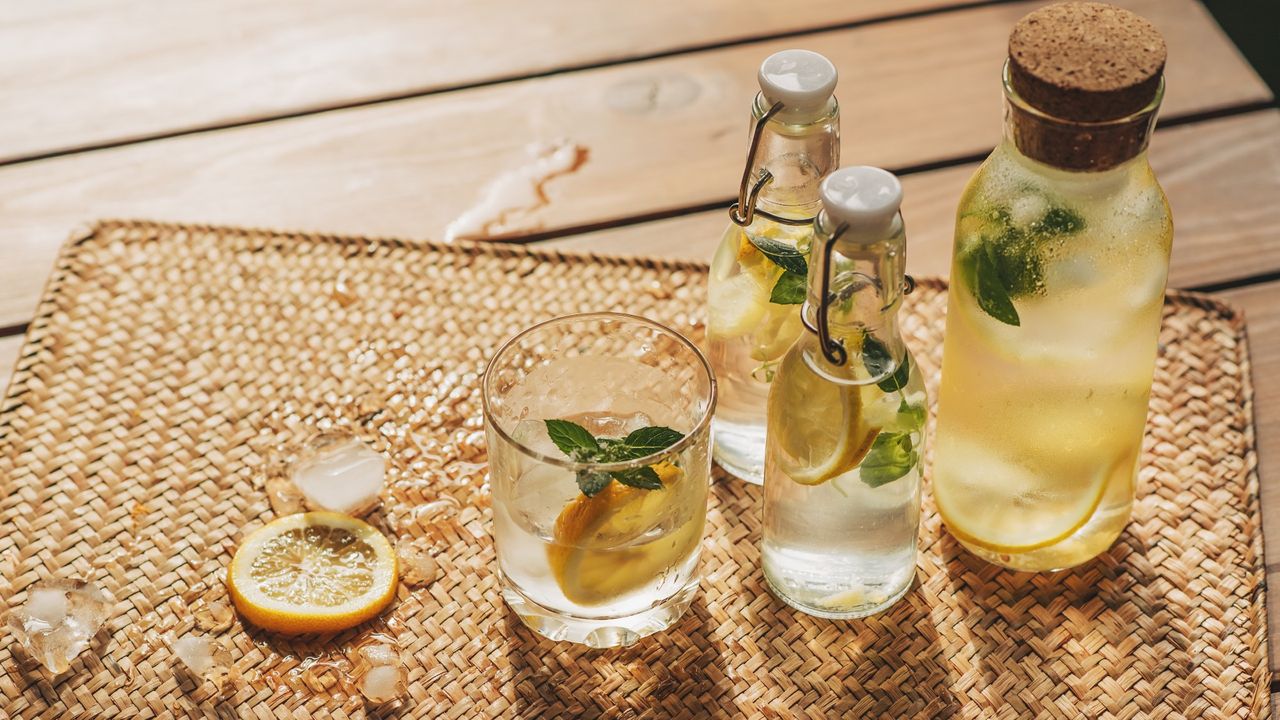 Bottles of spring cocktails with orange slices sitting on a table in the sunlight