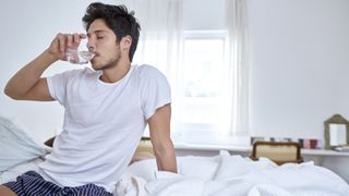 Man sitting in bed drinking water