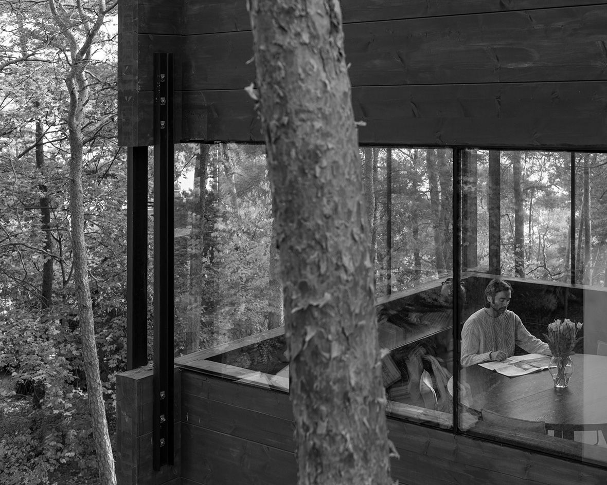 man sat at table seen from the outside through glass in modern cabin Villa Nikkesmelle by Gartnerfuglen
