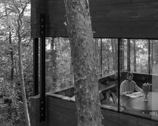 man sat at table seen from the outside through glass in modern cabin Villa Nikkesmelle by Gartnerfuglen