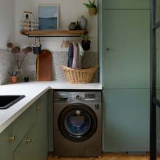 Utility room with green cabinets and white worktop, and a grey washing machine with clothes hanging above it