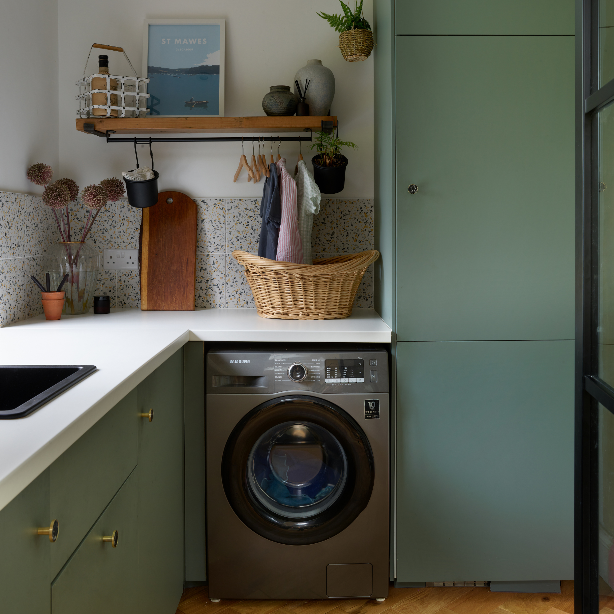Utility room with green cabinets and white worktop, and a grey washing machine with clothes hanging above it