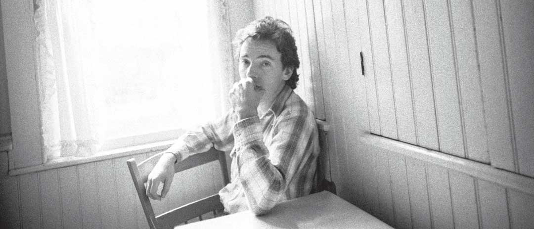 Bruce Springsteen seated at a kitchen table looking pensive