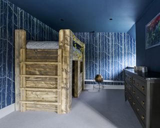 A kids bedroom with a loft bed and blue forest-inspired wallpaper