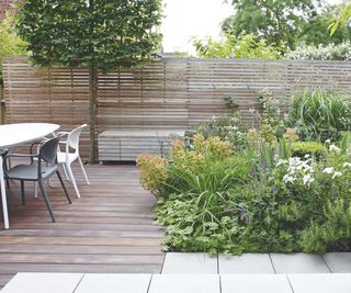 A contemporary outdoor garden with a slatted wooden fence with matching decking and a large garden bed