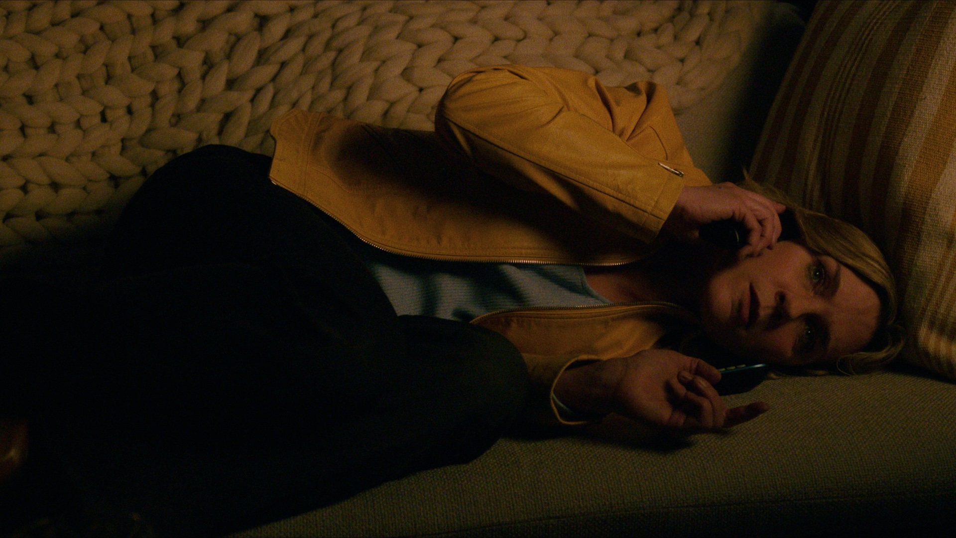 Rhea Seehorn in Pluribus laying on a coach whilst on the phone