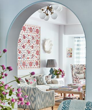 living room with white walls, pale blue arch, patterned armchairs and cushions and suzani on the wall