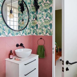 a pink tiled bathroom with a leafy green wallpaper